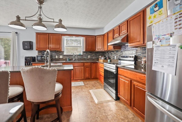 kitchen with appliances with stainless steel finishes, a kitchen breakfast bar, dark stone counters, a kitchen island with sink, and decorative light fixtures