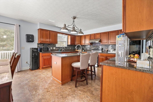 kitchen with sink, dark stone counters, decorative light fixtures, a kitchen island with sink, and a breakfast bar