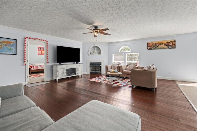 living room with a textured ceiling, ceiling fan, a fireplace, and dark wood-type flooring