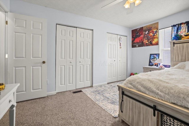 carpeted bedroom with ceiling fan, a textured ceiling, and two closets