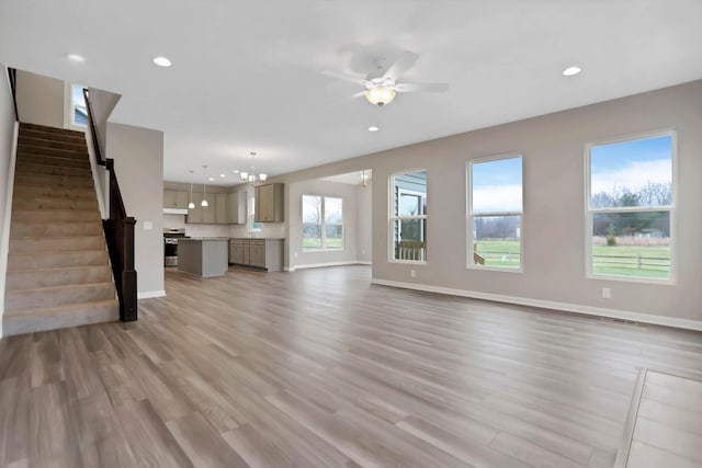 unfurnished living room featuring ceiling fan with notable chandelier and light hardwood / wood-style flooring