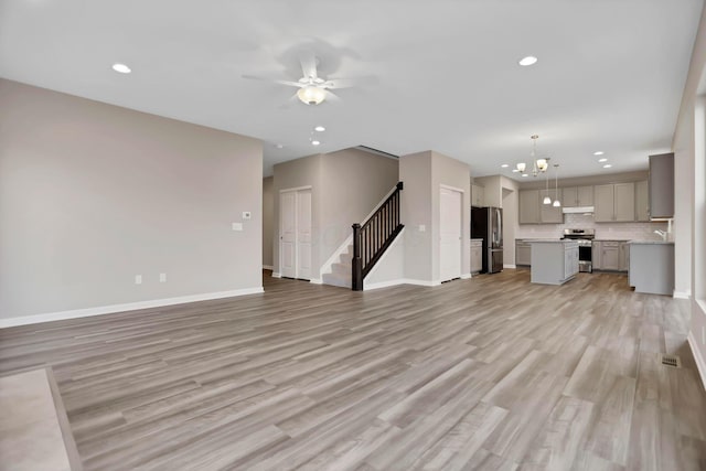 unfurnished living room featuring light wood-type flooring and ceiling fan with notable chandelier