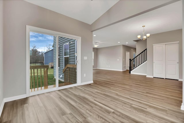 spare room featuring ceiling fan with notable chandelier, light wood-type flooring, and lofted ceiling