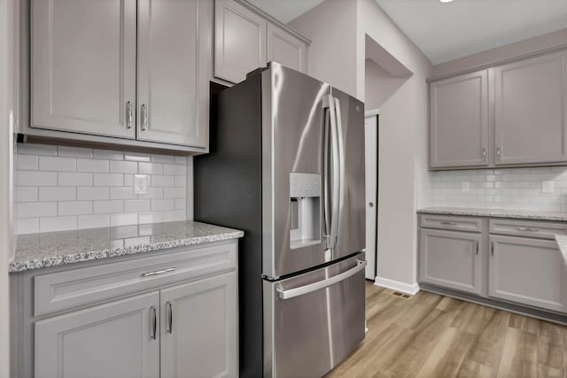 kitchen with light stone countertops, stainless steel refrigerator with ice dispenser, tasteful backsplash, and light hardwood / wood-style flooring