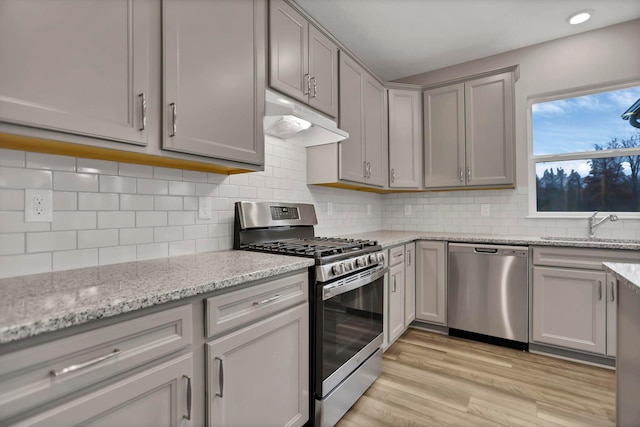 kitchen with sink, light stone countertops, light wood-type flooring, tasteful backsplash, and stainless steel appliances