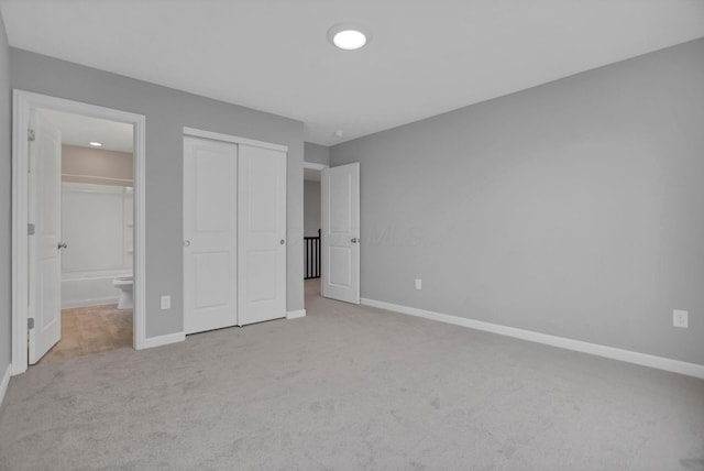 unfurnished bedroom featuring light carpet, ensuite bathroom, and a closet