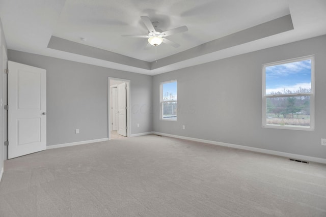 spare room featuring ceiling fan, light carpet, a wealth of natural light, and a tray ceiling