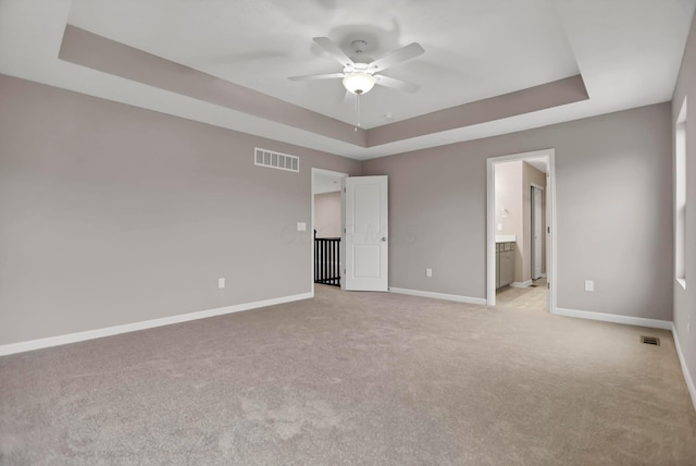 unfurnished bedroom featuring a raised ceiling, connected bathroom, ceiling fan, and light carpet