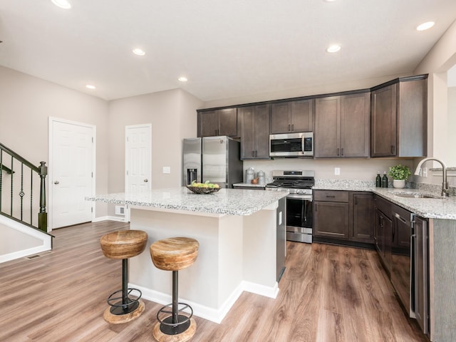 kitchen with hardwood / wood-style floors, sink, light stone countertops, appliances with stainless steel finishes, and a kitchen island