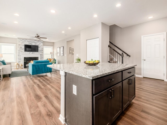 kitchen featuring dark brown cabinetry, ceiling fan, a stone fireplace, and light wood-type flooring