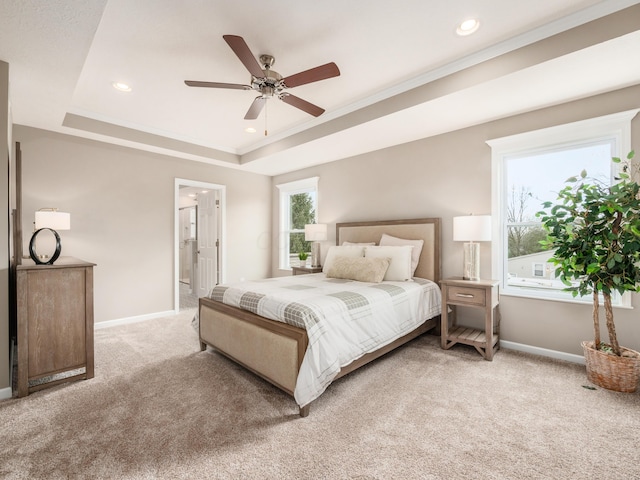 carpeted bedroom with a tray ceiling, ceiling fan, ornamental molding, and ensuite bathroom