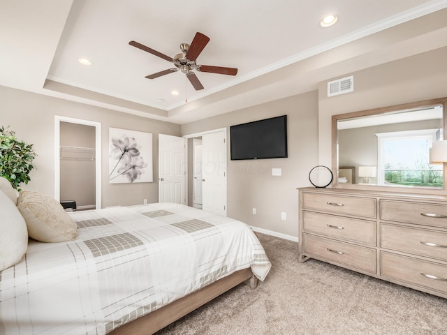 bedroom featuring light carpet, a walk in closet, ceiling fan, a tray ceiling, and a closet