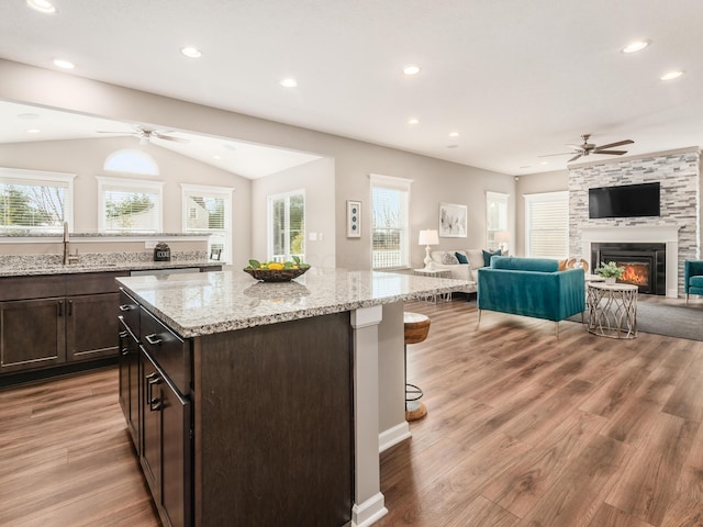 kitchen with a breakfast bar, a stone fireplace, sink, light wood-type flooring, and a kitchen island