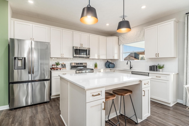 kitchen with white cabinetry, sink, hanging light fixtures, stainless steel appliances, and a kitchen island