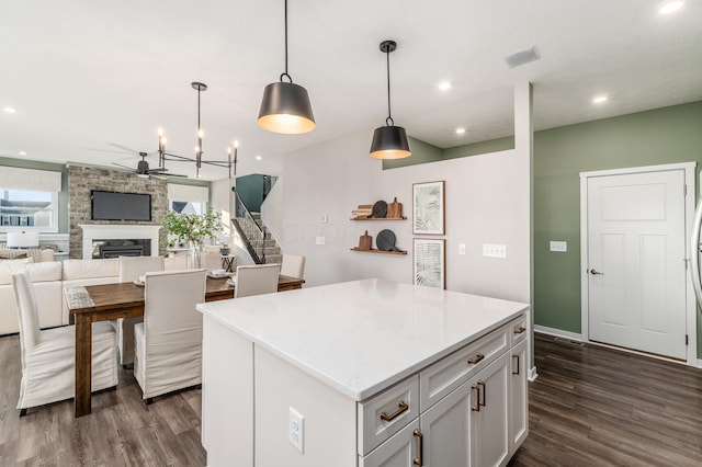 kitchen featuring a stone fireplace, a kitchen island, dark wood-type flooring, and decorative light fixtures