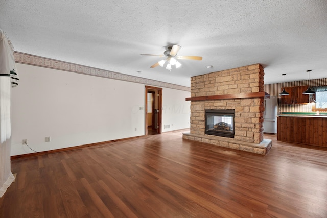 unfurnished living room with a stone fireplace, ceiling fan, wood-type flooring, and a textured ceiling