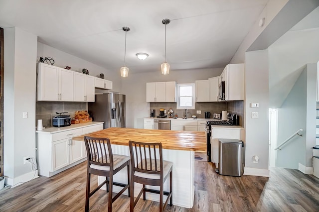 kitchen with wooden counters, appliances with stainless steel finishes, pendant lighting, white cabinets, and a center island