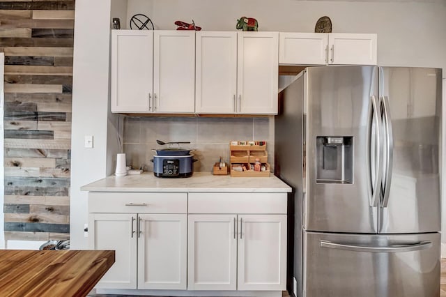 kitchen featuring decorative backsplash, stainless steel fridge with ice dispenser, white cabinets, and light stone counters