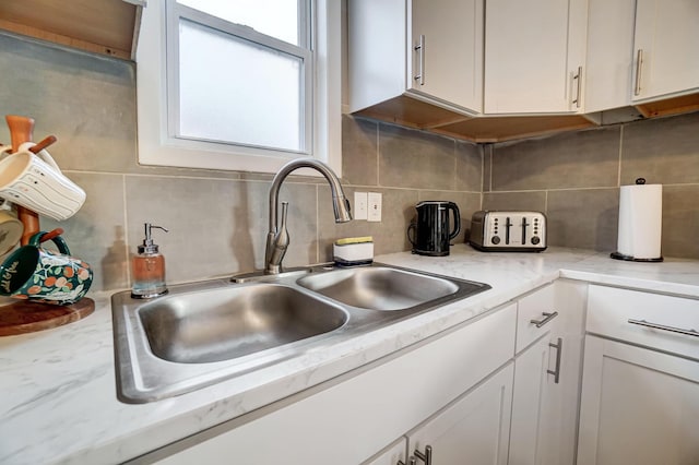 kitchen with light stone counters, tasteful backsplash, white cabinetry, and sink