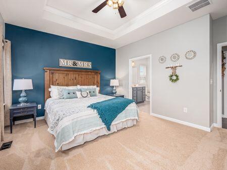 bedroom featuring carpet floors, a tray ceiling, ensuite bath, and ceiling fan