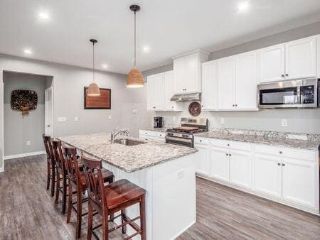 kitchen with white cabinetry, sink, decorative light fixtures, a kitchen island with sink, and appliances with stainless steel finishes