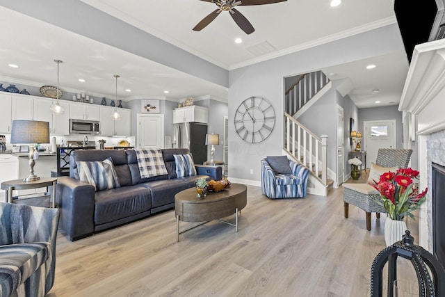 living room featuring ornamental molding, light hardwood / wood-style flooring, ceiling fan, and a stone fireplace