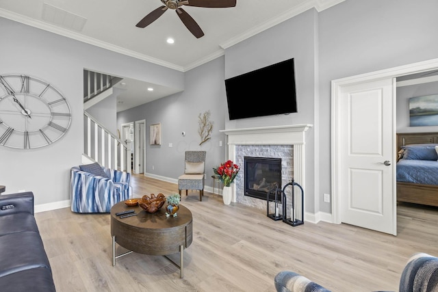 living room featuring ceiling fan, a stone fireplace, light wood-type flooring, and crown molding