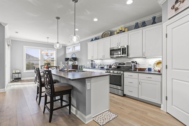 kitchen with sink, hanging light fixtures, a kitchen island with sink, white cabinets, and appliances with stainless steel finishes