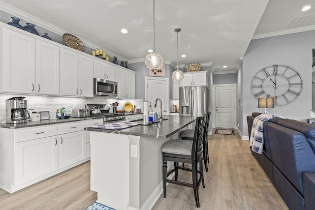 kitchen with decorative backsplash, stainless steel appliances, decorative light fixtures, white cabinetry, and an island with sink