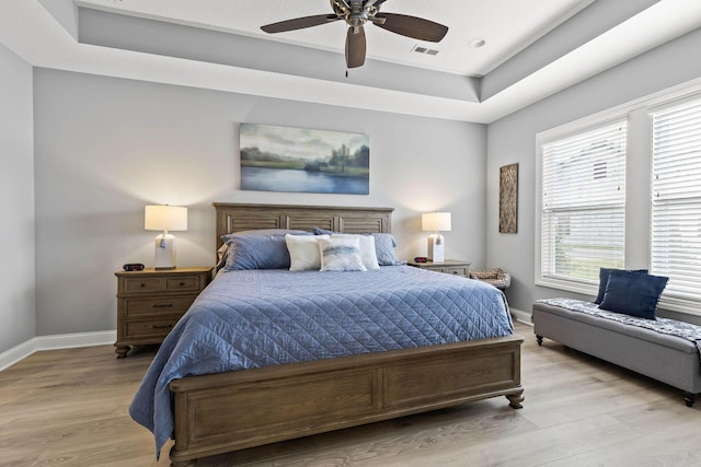 bedroom featuring a raised ceiling, ceiling fan, and light hardwood / wood-style flooring