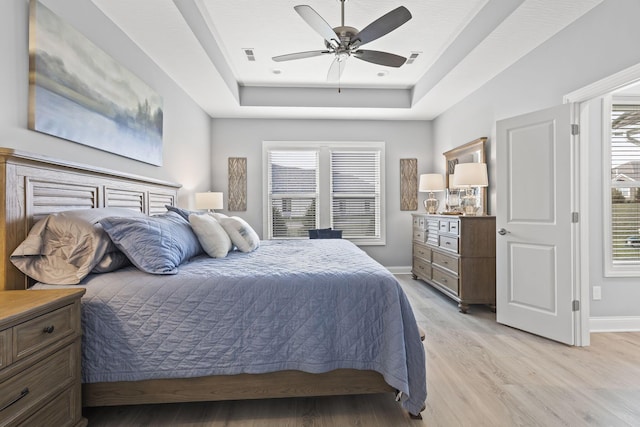 bedroom with ceiling fan, light wood-type flooring, multiple windows, and a tray ceiling