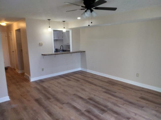 unfurnished living room featuring dark hardwood / wood-style floors, ceiling fan, and sink