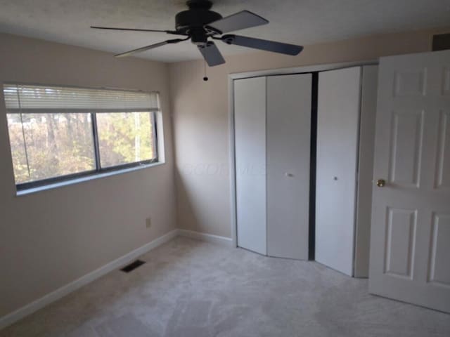 unfurnished bedroom featuring light carpet, a closet, and ceiling fan