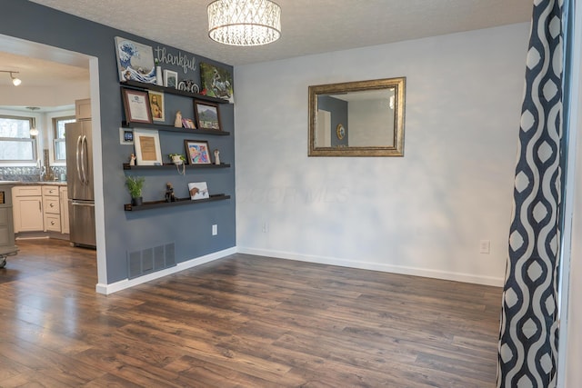 empty room with a textured ceiling, dark hardwood / wood-style floors, and a notable chandelier