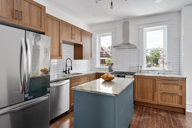 kitchen with a center island, wall chimney range hood, sink, light stone countertops, and appliances with stainless steel finishes