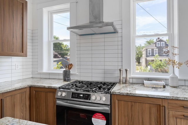 kitchen with stainless steel gas range oven, decorative backsplash, wall chimney exhaust hood, and a healthy amount of sunlight