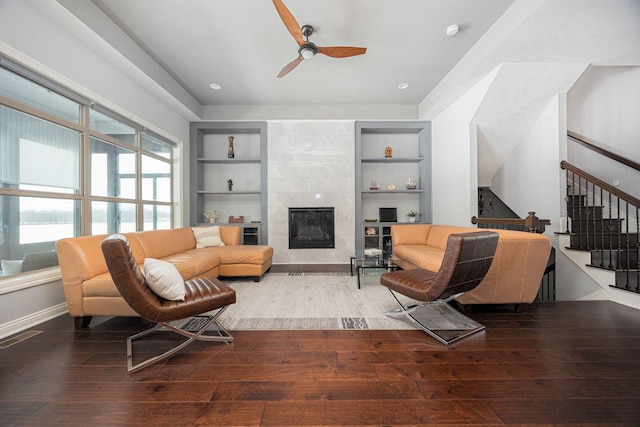 living room with ceiling fan, wood-type flooring, built in features, and a tiled fireplace