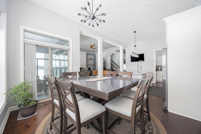 dining space with ceiling fan with notable chandelier, dark wood-type flooring, and decorative columns