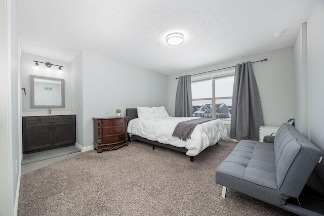 bedroom with ensuite bathroom, sink, carpet floors, and a textured ceiling