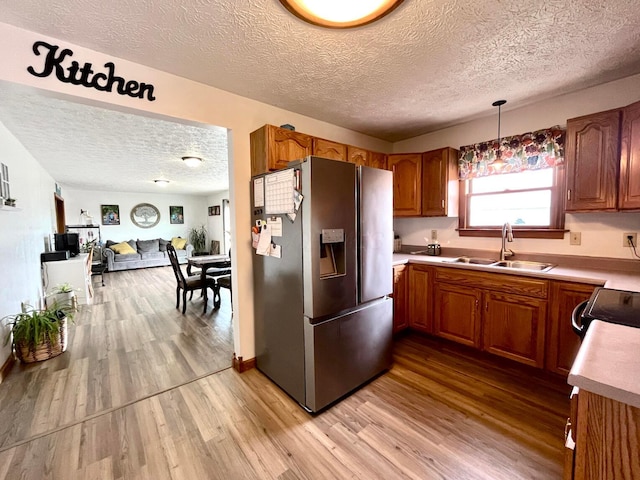 kitchen with stainless steel fridge with ice dispenser, decorative light fixtures, light hardwood / wood-style floors, and sink