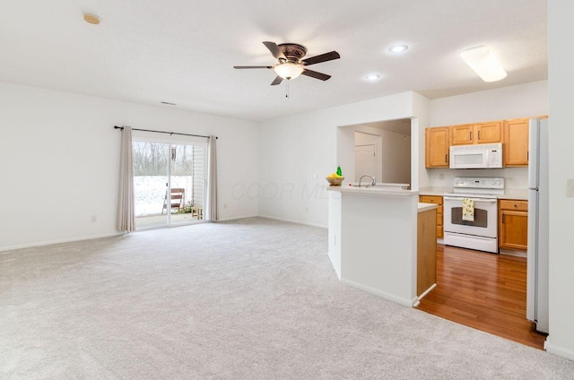 kitchen with light carpet, light brown cabinetry, white appliances, ceiling fan, and a center island with sink