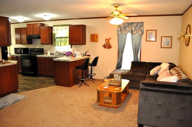 kitchen featuring a kitchen breakfast bar, dark carpet, ceiling fan, crown molding, and black appliances