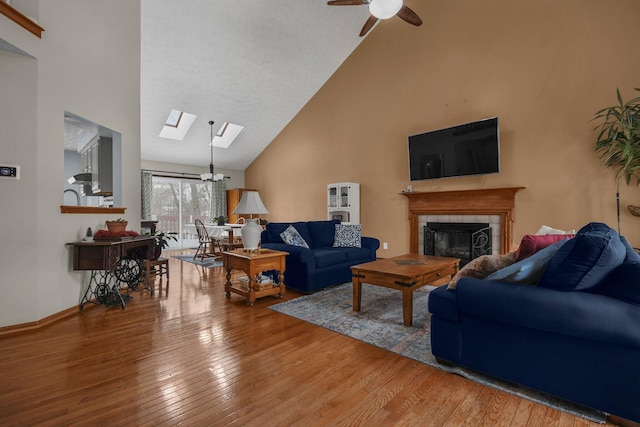 living room featuring a skylight, ceiling fan, high vaulted ceiling, wood-type flooring, and a fireplace