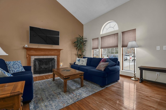 living room featuring hardwood / wood-style floors, high vaulted ceiling, and a tiled fireplace