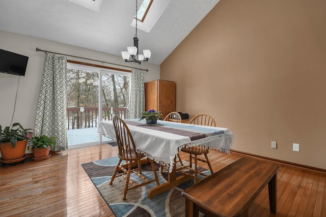 dining area with vaulted ceiling with skylight, a textured ceiling, hardwood / wood-style flooring, and a chandelier