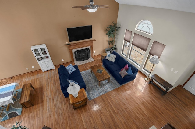 living room featuring a tiled fireplace, ceiling fan, a high ceiling, and hardwood / wood-style flooring