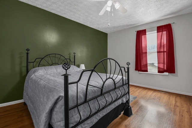 bedroom with ceiling fan, wood-type flooring, and a textured ceiling