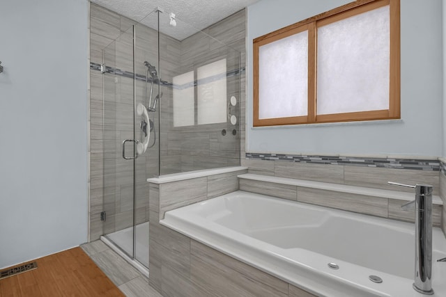 bathroom featuring plus walk in shower, wood-type flooring, and a textured ceiling