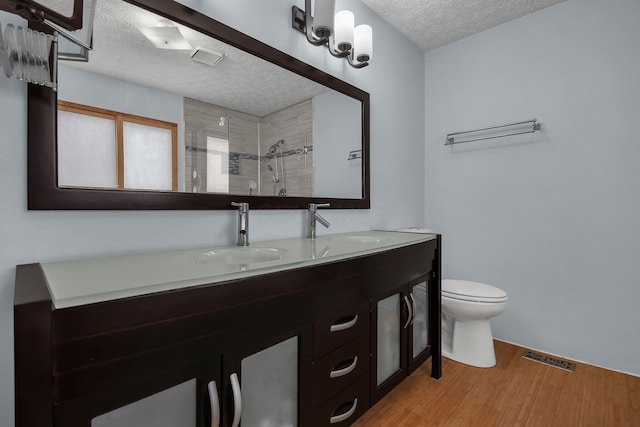 bathroom with a textured ceiling, vanity, a shower, wood-type flooring, and toilet