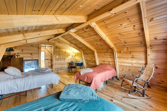 bedroom featuring wooden walls, light hardwood / wood-style flooring, vaulted ceiling with beams, a barn door, and wood ceiling